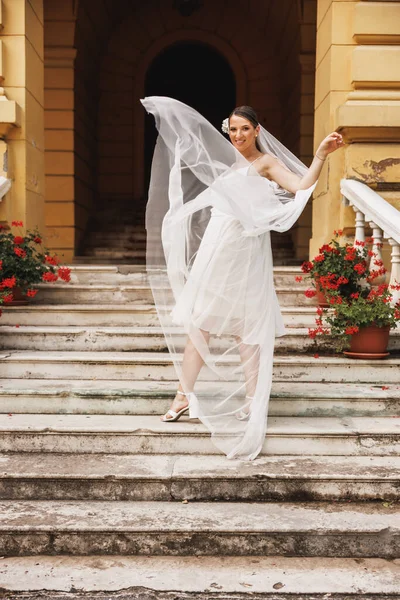美丽的新娘在户外的楼梯上玩乐 而新娘的婚纱在空中飘扬 — 图库照片