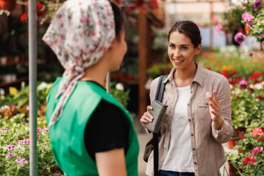 Genç bayan bitki yetiştirme gönüllüsü çiçekleri seçen ve satın alan genç bir kadına yardım ediyor..