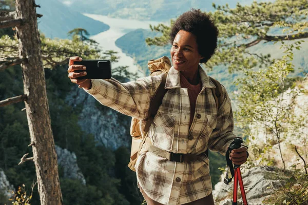 丘の上に立ち 山の中でハイキング中に景色を楽しみながら自撮りをする熟女 — ストック写真