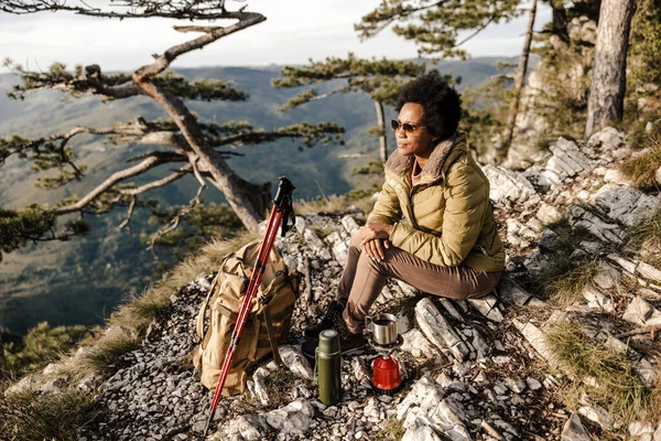 山の中でハイキング中に丘の上に座ってお茶を飲む成熟した黒人女性 — ストック写真