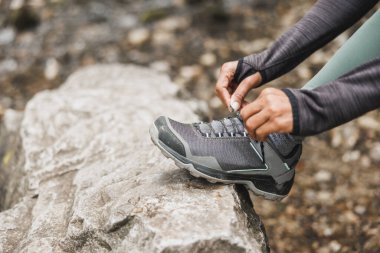 Yürüyüş yaparken ya da dağda koşarken spor ayakkabılarını bağlayan tanınmamış siyahi bir kadının yakın çekimi..