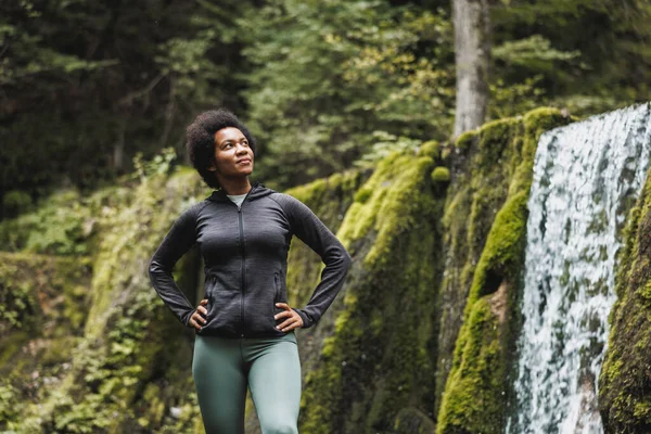 山の中を探検しながら滝の近くで楽しむ成熟したアフリカ系アメリカ人女性 — ストック写真