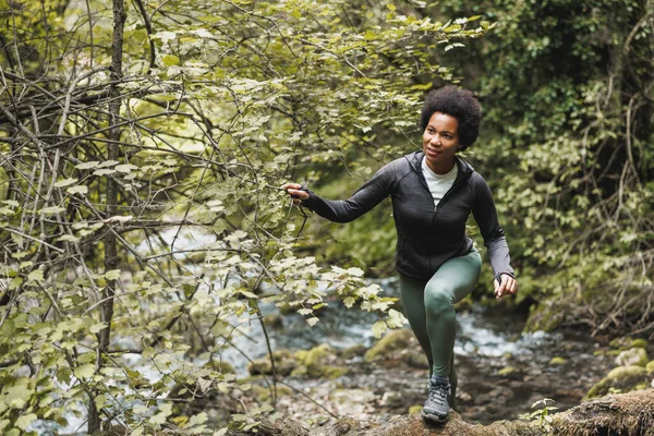 成熟したアフリカ系アメリカ人の女性ハイカーは 山の中を探索しながら川を渡り 屋外トレーニングを楽しむ — ストック写真
