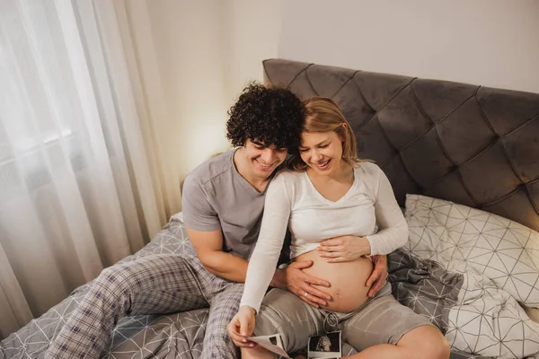 幸せな期待しているカップル見ますで彼らの赤ちゃんの医療スキャンでリラックスしながらベッドでベッド — ストック写真