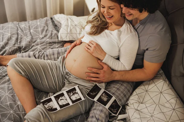 幸せな期待しているカップル見ますで彼らの赤ちゃんの医療スキャンでリラックスしながらベッドでベッド — ストック写真