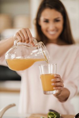 Mutfağına taze portakal suyu döken gülümseyen genç bir kadının fotoğrafı. Seçici odak.