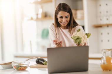 Evde sağlıklı bir yemek hazırlarken dizüstü bilgisayar kullanarak video blogu yapan genç bir kadının fotoğrafı..