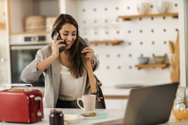 Birden fazla işi olan genç bir iş kadınının akıllı telefondan konuşması ve işe gitmeye hazırlanırken evde kahvaltı etmesi..