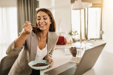 Evde dizüstü bilgisayar kullanırken gülümseyen bir kadının fotoğrafı..