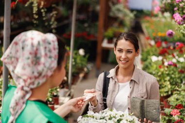 Genç bir kadın bahçe merkezinden genç bir girişimciden çiçek alıyor..