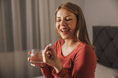 Elinde su bardağı olan hamile bir kadın ve evde doğum öncesi vitamin hapı içiyor..