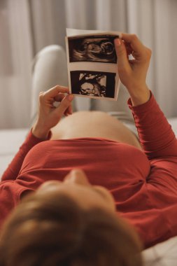 Müstakbel anne yatak odasında yatağında dinlenirken bebeğinin ultrasonuna bakıyor..