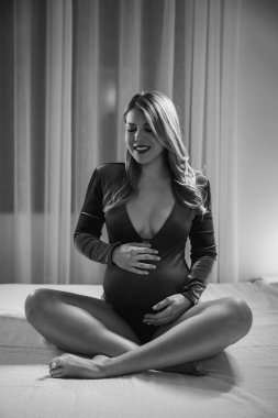 Yatak odasındaki yatakta dinlenirken kadın iç çamaşırı giymeyi bekliyor. Siyah ve beyaz.