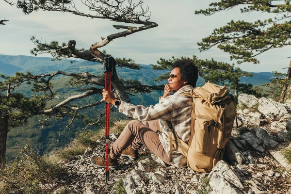 ハイキング中に山の崖の上に座りながら景色を楽しむ熟女 — ストック写真
