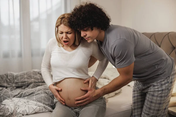 Doğum sancısı çeken hamile karısına yatak odasında yardım eden endişeli bir adam..