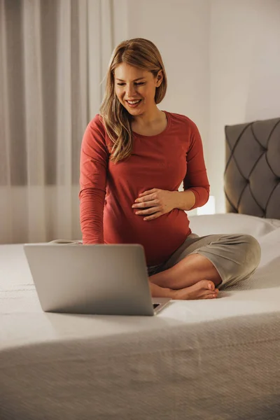ベッドルームのベッドでリラックスしながら ラップトップでビデオ通話をする幸せな妊婦 — ストック写真