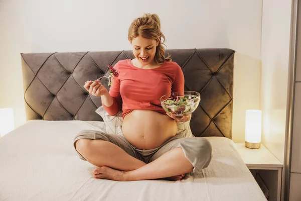 彼女の寝室のベッドに座っている間に新鮮な野菜サラダを食べる女性を期待して幸せ — ストック写真