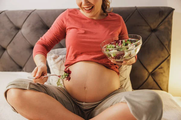 ベッドの上に座っている間に新鮮な野菜サラダを食べる女性を期待して認識できない幸せの近く — ストック写真