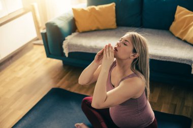 Genç hamile bir kadın sabahları evde yoga yapıyor. Oturma odasında esneme egzersizi yapıyor..