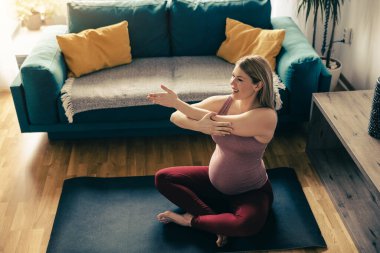 Genç hamile bir kadın sabahları evde yoga yapıyor. Esneme egzersizi yapıyor..