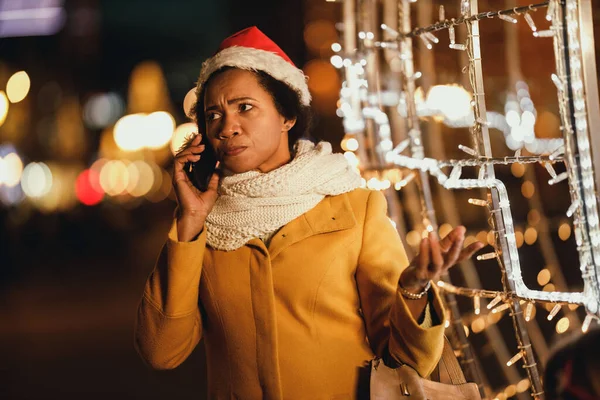 Middle age worried black woman talking on her smartphone at festive Christmas night in the city.