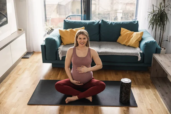 年轻的孕妇早上在家里锻炼 她在运动垫上锻炼 看着镜头 — 图库照片