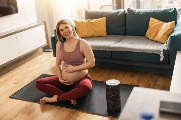 年轻的孕妇早上在家里锻炼 她在运动垫上放松下来 看着镜头 — 图库照片