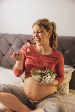 Mutlu bir kadın yatak odasında yatağında oturmuş taze sebze salatası yiyor..