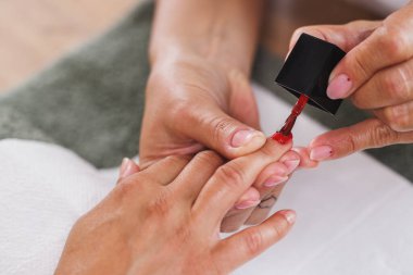 Bir güzellik salonunda manikür yaparken kırmızı oje sürerken tanınmayan bir güzellik uzmanının kesilmiş görüntüsü..