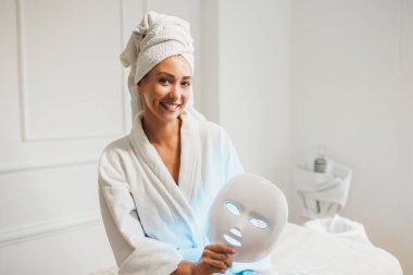 Güzel genç bir kadın güzellik salonunda yüzü için öncü ışık terapisi maskesi yaptırıyor..