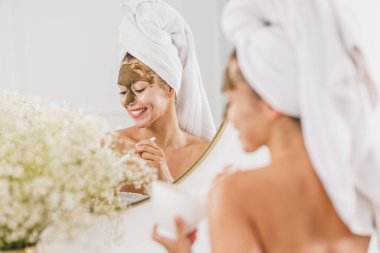 Aynanın karşısına geçip evdeki banyoya yüz maskesi takan güzel genç bir kadın..