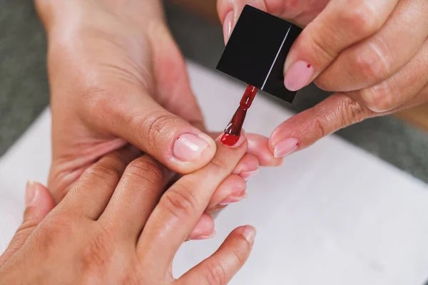 stock image Cropped image of an unrecognizable beautician applying red nails polish to woman during manicure treatment in a beauty salon.