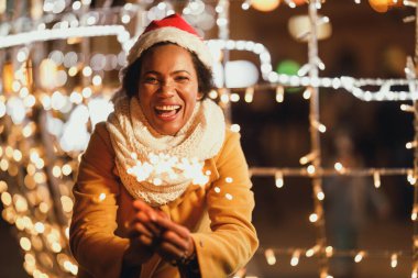 Orta yaşlı, siyah bir kadın şehirde kış gecesinde maytap tutuyor..