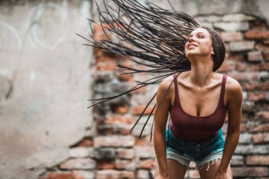Uzun afro örgülü saçlı neşeli beyaz kadın tuğla duvara karşı eğleniyor..