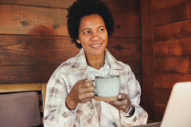 Siyah kadın, tatilini rahat, ahşap bir evde geçirirken sabah çayı içiyor..