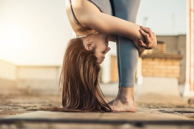Relaxed woman practicing yoga stretching exercise on a rooftop terrace at sunset.