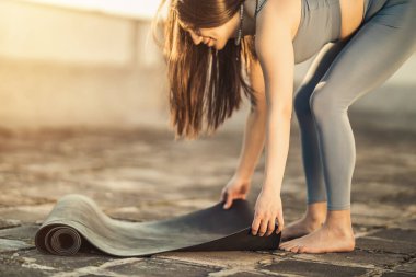 Rahat kadın gün batımında terasta yoga çalışmak için egzersiz minderi hazırlıyor..