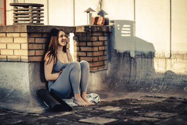 Genç bayan gün batımında terasta yoga eğitimine hazırlanırken bir şeyler düşünüyor..