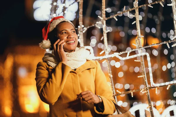 Middle age African woman talking on smartphone and having fun in the city street at Christmas time.