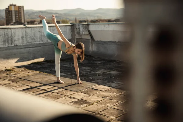 Female teenager practicing yoga on a rooftop terrace.