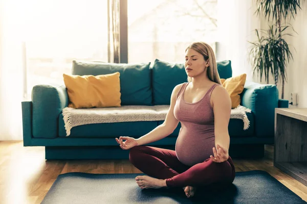 年轻的孕妇在家里锻炼 她在运动垫上锻炼 在客厅里做瑜伽来增进自己的幸福 — 图库照片