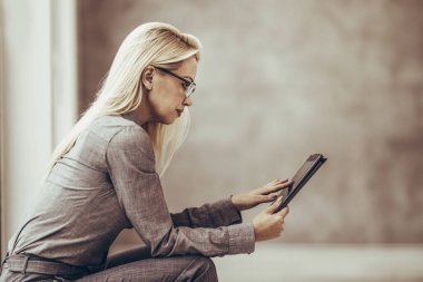 Mola sırasında ofisin penceresinin yanında otururken dijital tablet kullanan kendine güvenen bir iş kadını..