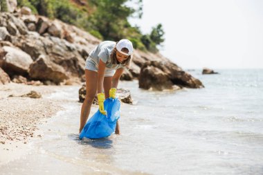 Plajı temizlemek için plastik torbaya çöp toplayan gönüllü bir genç..