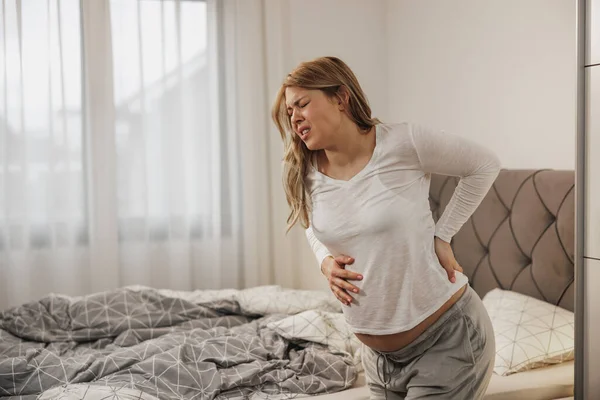 stock image Pregnant woman holding her stomach while having contractions in a bedroom. 