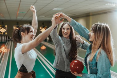 Three young happy women are celebrating their score in bowling club.