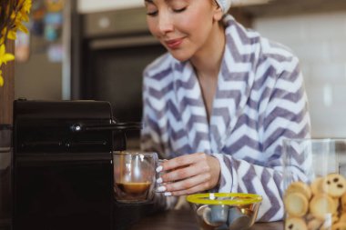 Evdeki mutfakta kahve makinesiyle kahve yapan bir kadının görüntüsü..