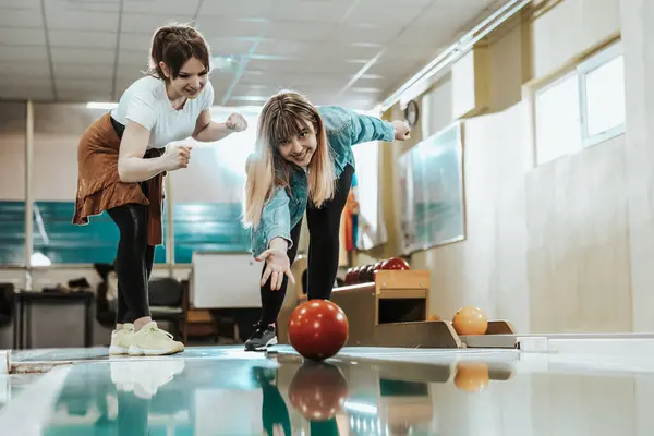 İki gülümseyen genç kadın bowling topunu fırlatırken ve birlikte vakit geçirirken eğleniyorlar..