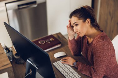 Evindeki bilgisayarla uğraşırken düşünceli görünen yaratıcı genç bir kadın..