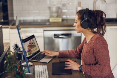 Kulaklıklı genç bayan girişimci ev ofisinden bilgisayarla çalışıyor..