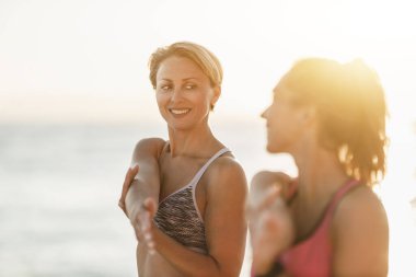 İki bayan arkadaş deniz kıyısında antrenman yaparken esneme egzersizleri yapıyorlar..